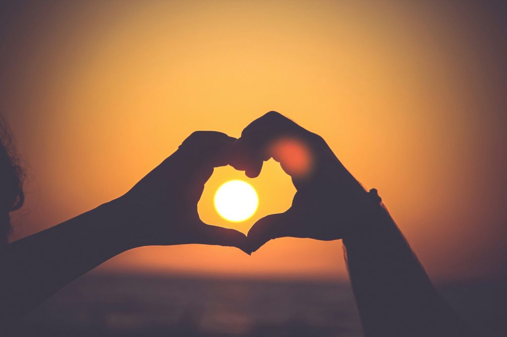 Hands forming a heart shape in front of a sunset