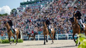 Scott Brash, Harry Charles and Ben Maher riding their horses on the lap of honour in front of the Paris 2024 crowds in Versailles with their medals around their necks.