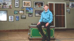 Harry Charles sitting on a trunk at home in front of a wall of pictures of his competing.