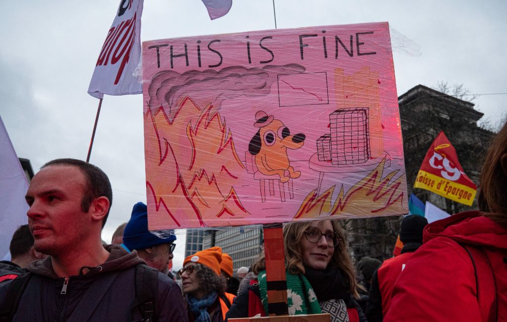 A demonstrator holds a sign with a meme saying "this is fine" on December 12, 2023 in Brussels, Belgium.