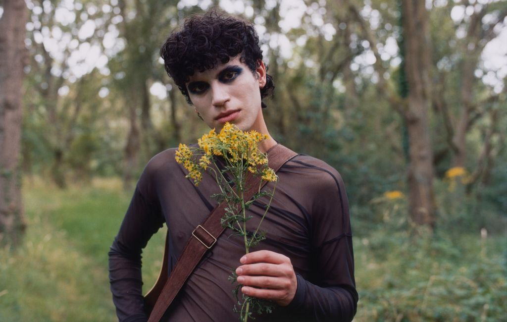 Jacob Alon pictured in nature with heavy makeup and a flower in their hand, photo by press