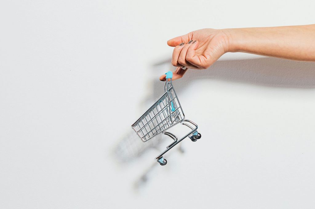 Against a white background, a person dangles a tiny shopping cart from their index finger