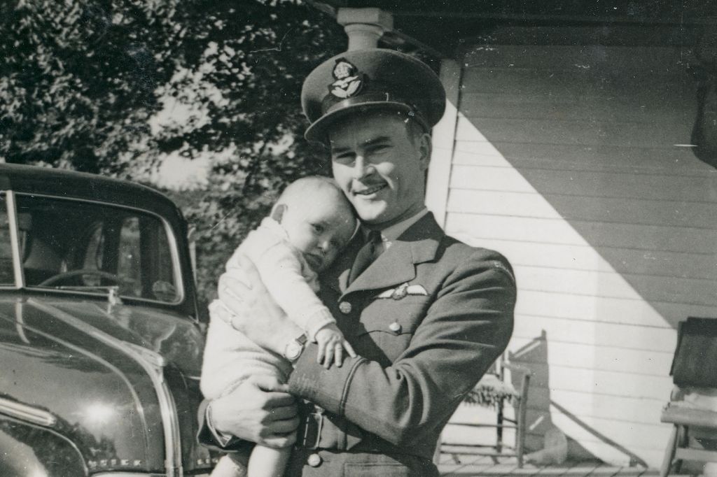 A black-and-white photograph of a man in a WWII pilot uniform, cuddling a baby.