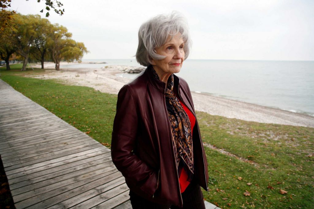 A photograph of Alice Munro on a board walk near a lake. She is looking away from the camera and wearing a jacket and scarf.