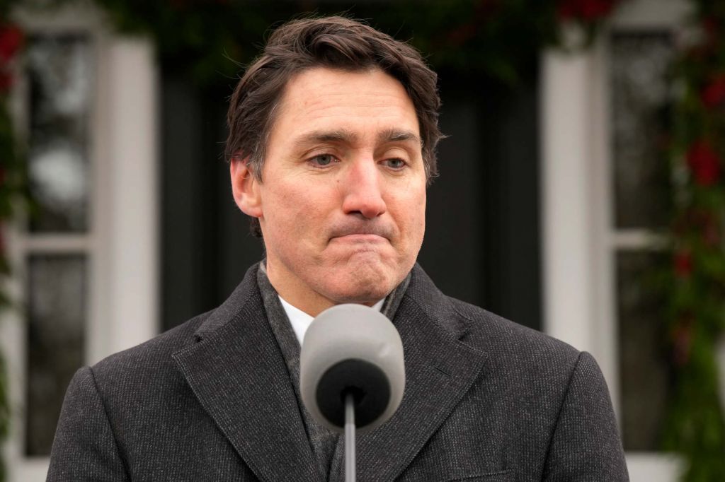 Prime Minister Justin Trudeau stands in front of a podium microphone and purses his lips into a frown