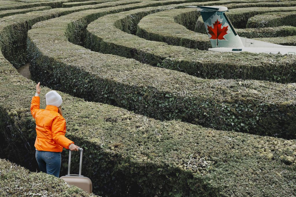 In a photo illustration, person in an orange jacket, holding onto the handle of a piece of luggage, flags a plane. They are separated from the plane by a tall hedge maze.