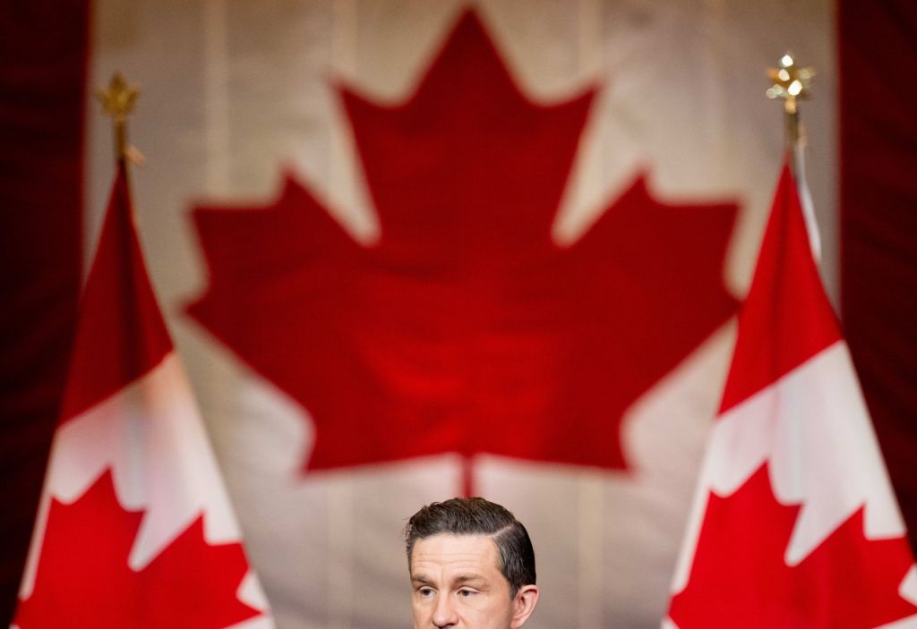 An image of conservative leader Pierre Poilievre speaking at a news conference with a Canadian flag behind him, but the bottom quarter of his face is cut off.