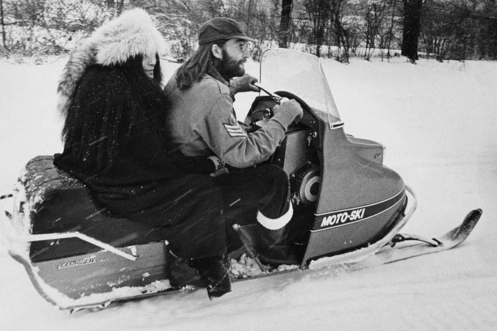 A black and white photo shows John Lennon and Yoko Ono on a snowmobile