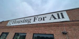 A Housing For All banner on a Toronto housing co-op with the one per cent logo from the 1998 campaign for all levels of government to allocate an additional one per cent of their budget to a national housing program.