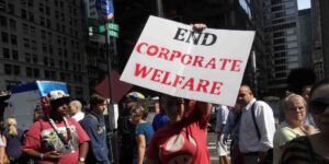 A woman holding a sign that reads "End Corporate Welfare."