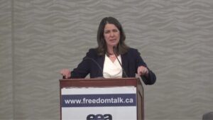 Danielle Smith stands at a podium at a libertarian conference on health care in the fall of 2021.