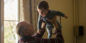 A grandfather lifts his grandchild up in the air.