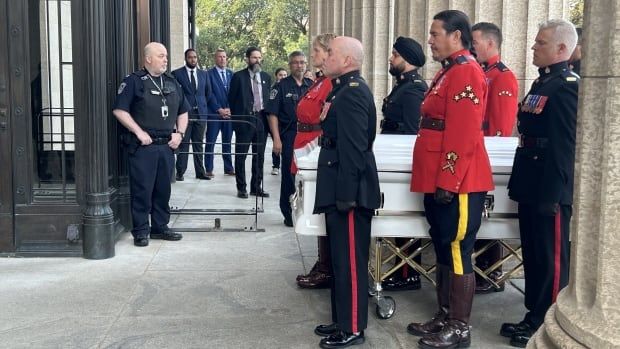 RCMP officers in red serge walk alongside a white casket.