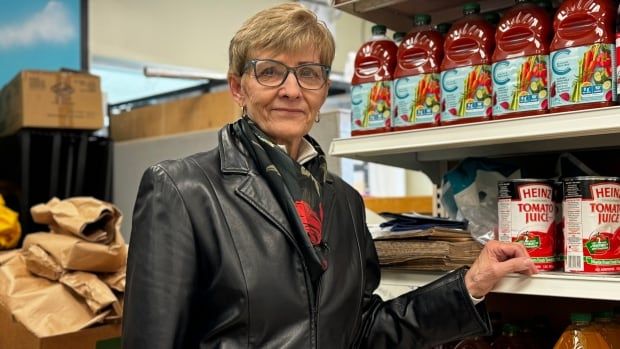 A woman wearing a black jacket and scarf is shown standing next to a shelf of juice.