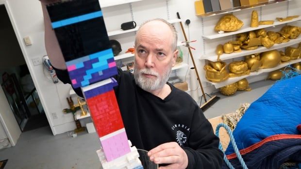 A man with a greying beard and wearing a black shirt places a piece of Lego atop a Lego tower