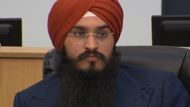 Close up photo of Gurpartap Singh Toor, wearing a blue jacket and orange turban, sitting in Brampton city council chambers. 