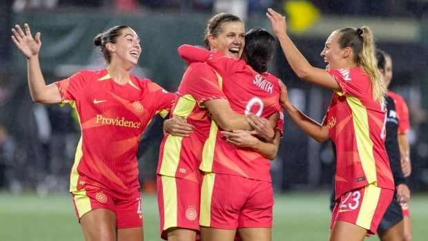 Soccer players wearing red jerseys hug in the rain.