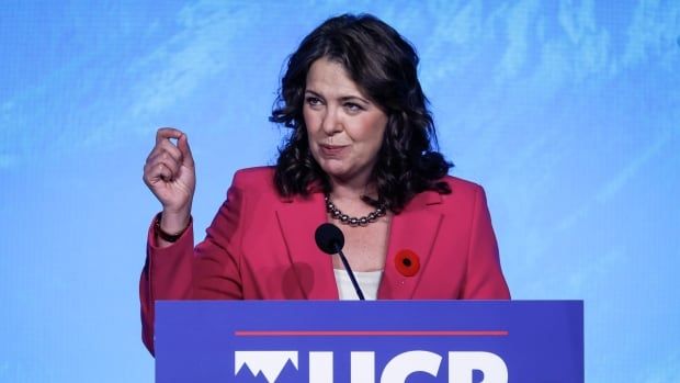 a woman gestures as she speaks at a lectern