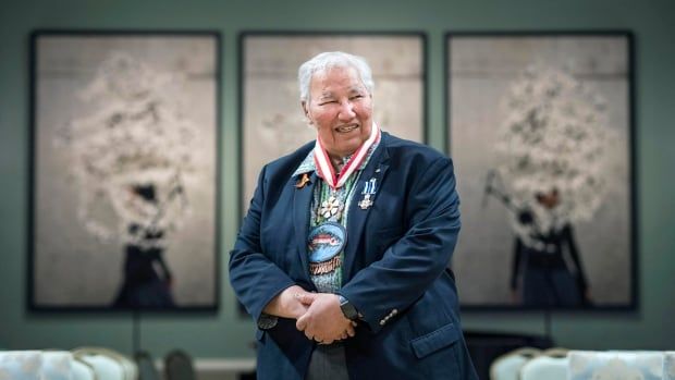 Smiling, Murray Sinclair looks off camera during a portrait of him, framed by three picture frames behind him.