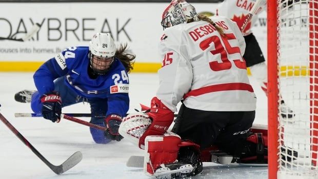 A women's hockey player falls to the ice while taking a shot on a goaltender.