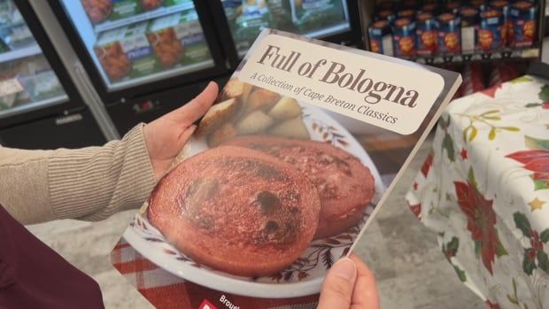 A pair of hands holds up a book called Full of Balogna: A Collection of Cape Breton Classics, featuring slices of fried baloney on a plate 