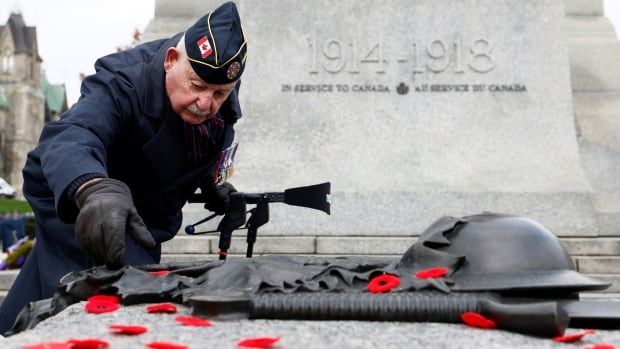 A military veteran puts a poppy pin on a war memorial. There are other pins on it already.