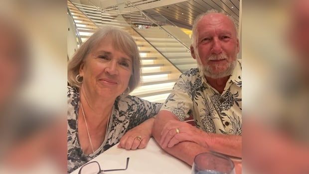 A couple in their 70s sitting for a photo in front of a set of stairs. 