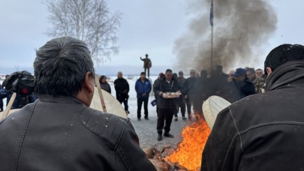 People gather around a fire, with some drumming 