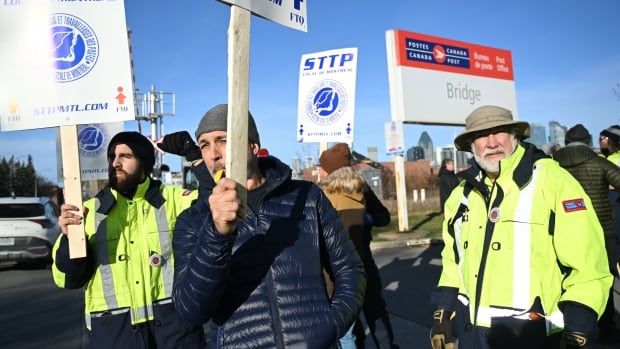 Workers bundled in winter jackets and toques picket outside a sorting plant on a clear day.