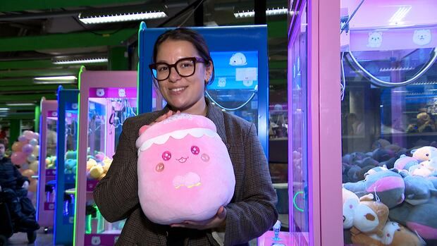 A woman holds a plush stuffed animal in her hands. She is standing in front of claw machines. 