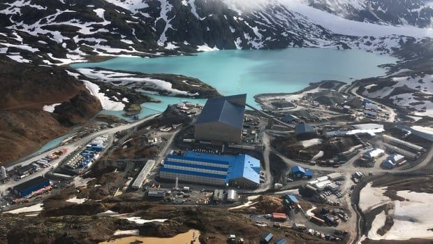 An aerial image shows a mine near a blue lake and snowy mountain valleys. 