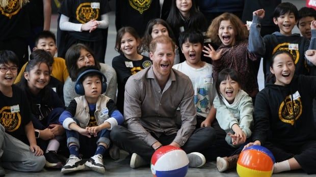 A man smiles and laughs in a group photo with a bunch of kids in black T-shirt school uniforms.