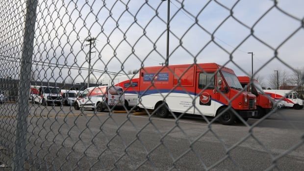 Canada Post vehicles behind a fence.