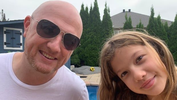 A man and his daughter pose for a picture in front of a pool. 