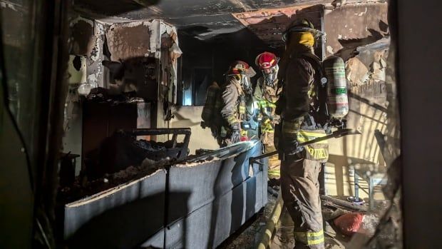 Three firefighters inside a dark, burnt home.