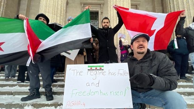 Three men are seeing in a crowd holding a sign and flags.