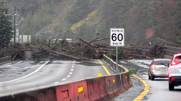 Logs block a highway in B.C. as vehicles wait.