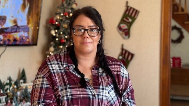 Woman with dark hair and glasses, stands in front of a room decorated for Christmas. 