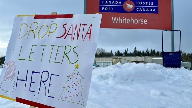 A sign reading Drop Santa Letters Here sits in front of a Canada Post sign.