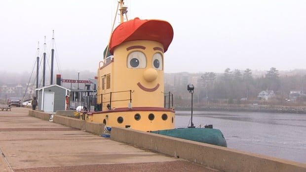 A yellow tugboat with a face and a red hat.