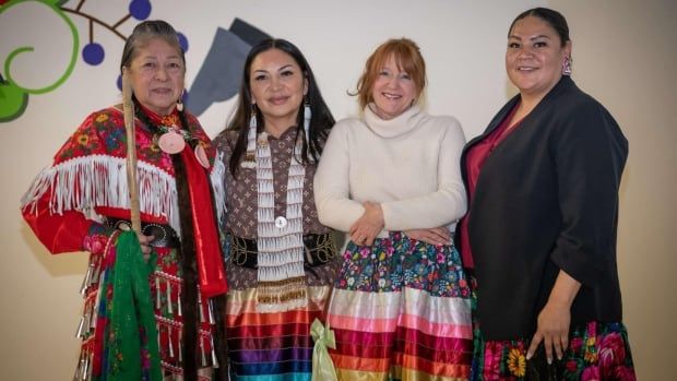 Four women pose for a photo in traditional and very colourful Indigenous ribbon skirts.