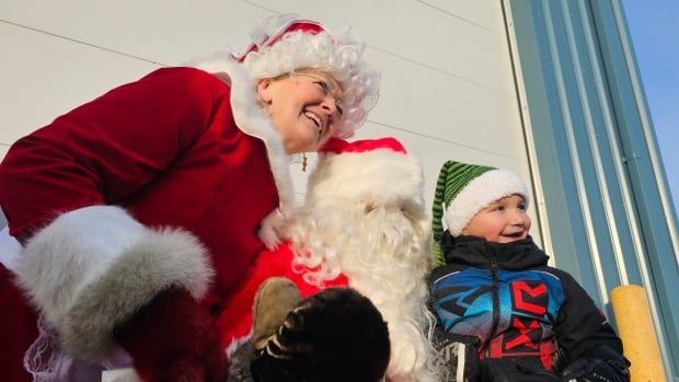 A smiling boy poses for a photo with Santa and Mrs. Claus.