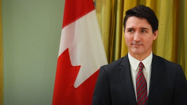 A man in a suit looks to the side while standing in front of a red and white flag. 