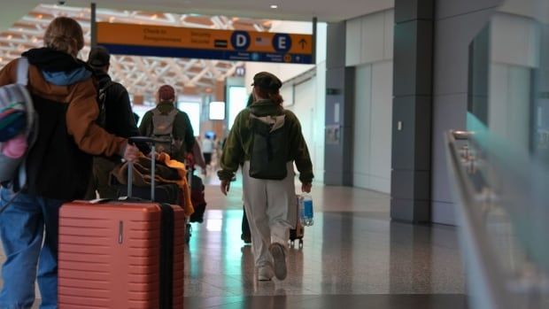 Several people pass through an airport with their luggage.