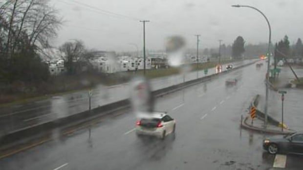 A traffic camera shows cars travelling along the road, with rain and water droplets visible on the camera.