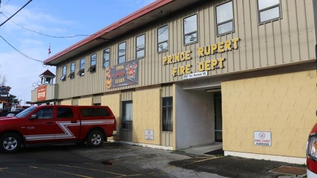 A building with text on it reading 'Prince Rupert Fire Dept', with a fire vehicle visible in a parking lot.