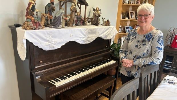 A woman with short grey hair standing next to a piano in a dining room.