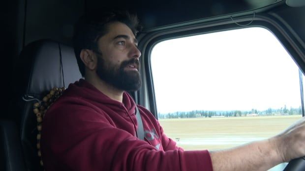 A bearded man in a red hoodie driving.