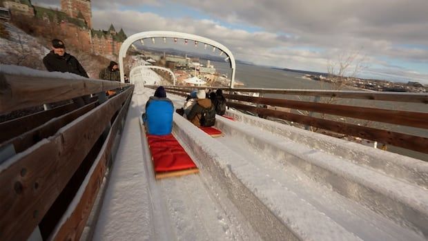 People sitting in toboggans with red cushions slide down the ice slide near Chateau Frontenac in Quebec City.