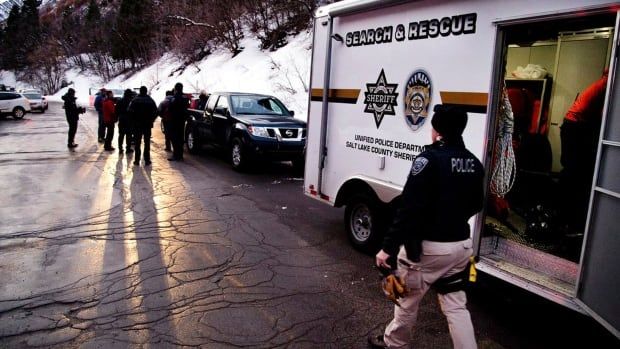 People gather around a truck that reads, 'Search and Rescue,' at the base of a snow hill.